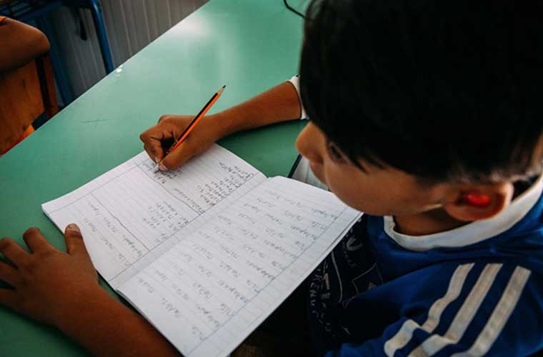 pojke skriver i bok mot grön bänk