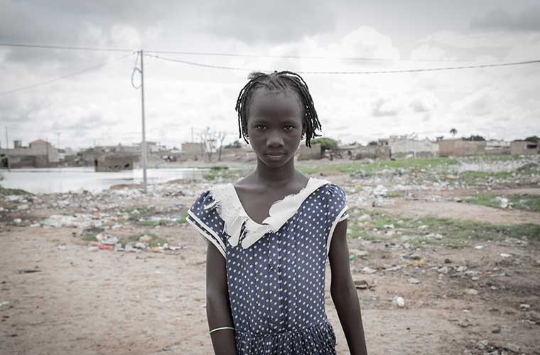 allvarlig flicka i blå klänning står utomhus framför sandvidder 