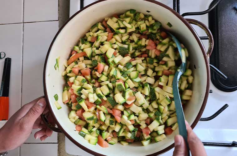vit kastrull på spis med hackade bitar av zucchini och tomater 