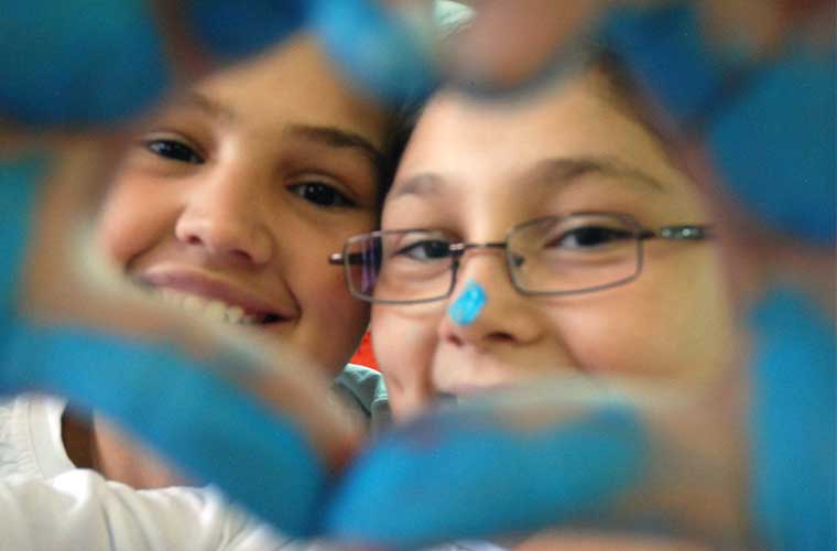  barn med glada ögon som tittar igenom ett hjärta format med en hand blå av målarfärg