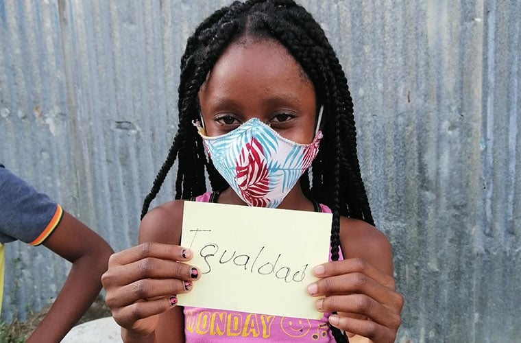 Flicka med munskydd håller en lapp där det står Igualdad