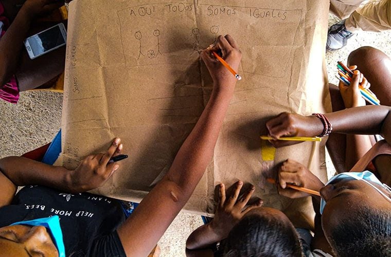 grupparbete där flera sitter runt ett stort papper och ritar streckgubbar