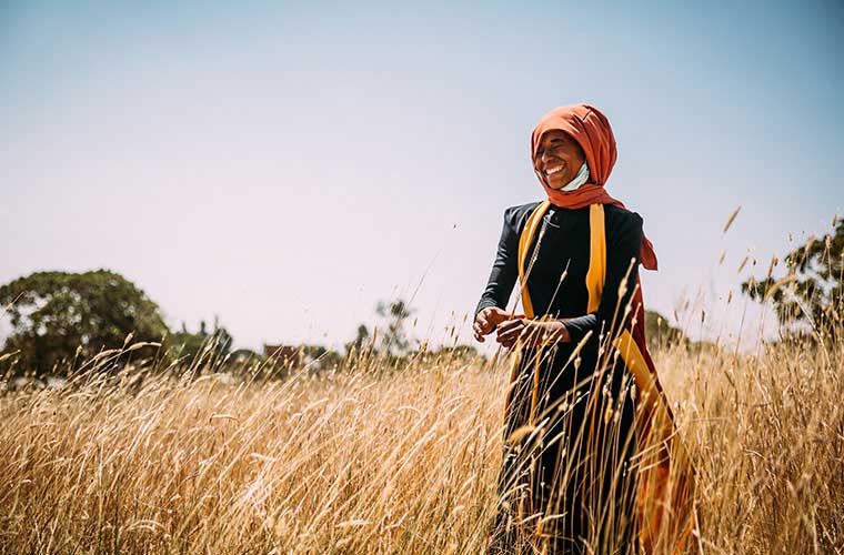 ung kvinna med orange huvudbonad står på ett fält och ler
