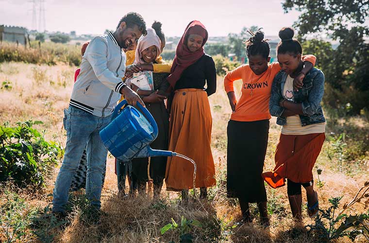 ungdomar står på ett fält och vattnar med vattenkanna