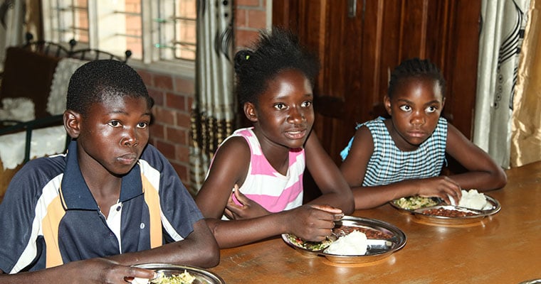 tre barn vid ett bord äter mat