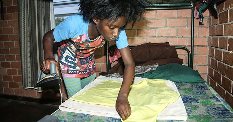 flicka stryker en gul skjorta med säng som strykbräda.